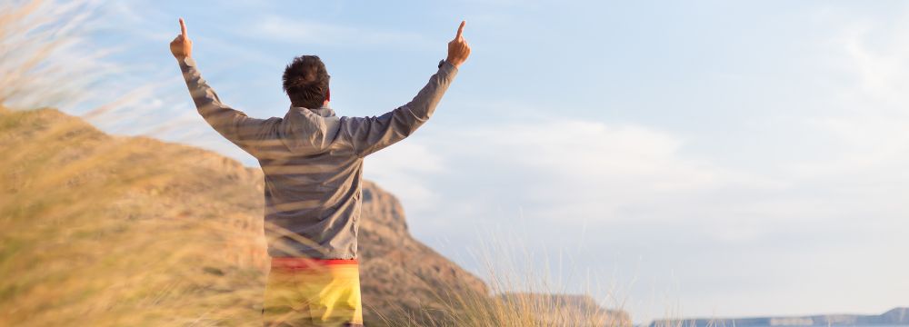 Man outside with both arms up looking over cliff