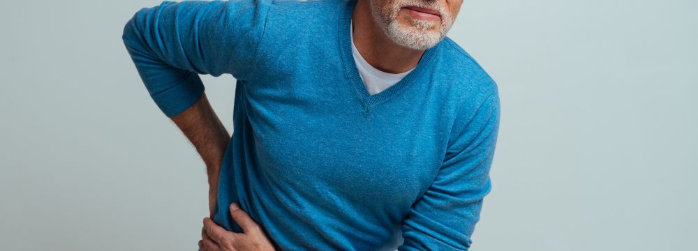 Older man with graying hair and bears holding side and back in pain