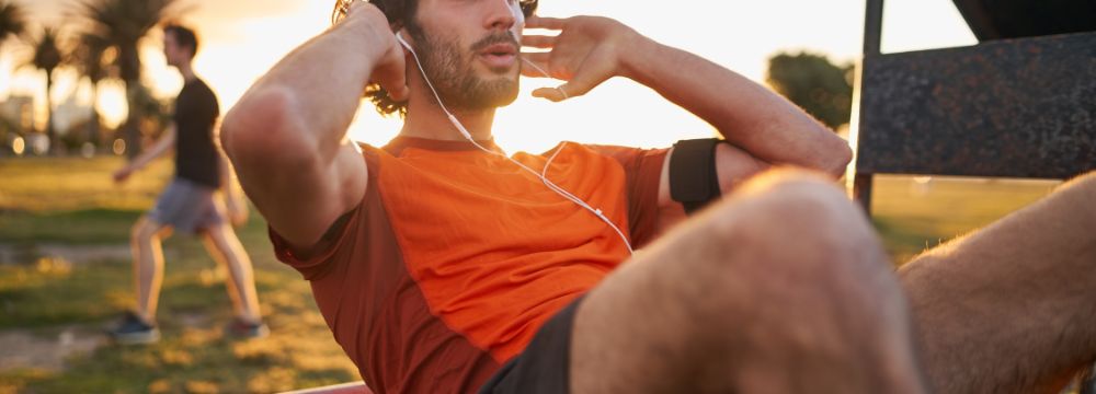 Younger man exercising in park with earbuds in 